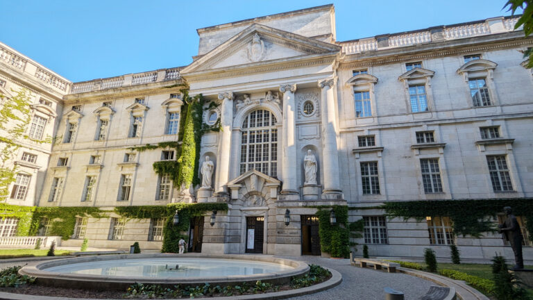 A minumental entrance to the State Library Berlin with a fountain in front.
