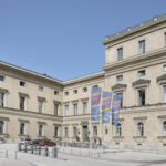 A plaza in front of a big building with flags showing the letters BAdW, which stand for Bavarian Academy of Sciences.