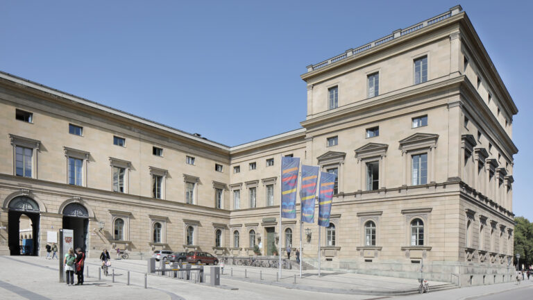 A plaza in front of a big building with flags showing the letters BAdW, which stand for Bavarian Academy of Sciences.