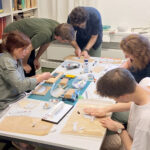 Five researchers rolling out cylinder seals on a table full of tools, baking paper and Fimo.