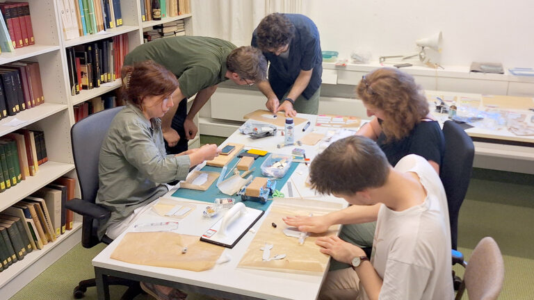 Five researchers rolling out cylinder seals on a table full of tools, baking paper and Fimo.