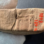 A close-up of a sealed envelope with visible cuneiform script and two figures. The right one is leading the left one to the right.